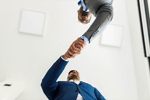 Low angle view of male entrepreneurs shaking hands after reaching an agreement in the office. Focus is on hands. Copy space.
