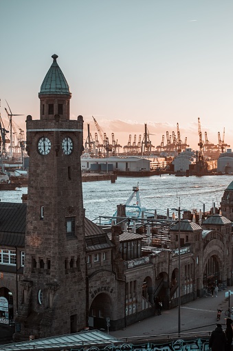 A picturesque view of a historic clock tower situated at a port, with several large ships in the background in Hamburg