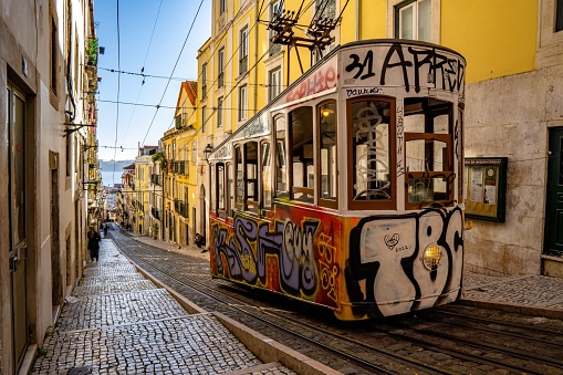 Lisboa, Portugal – September 12, 2022: A colorful graffiti-covered trolley parked on a narrow cobblestone street in Lisboa, Portugal