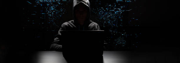 Computer hacker in black mask and hoodie. Obscured dark face. Data thief, internet fraud, cyber security concept.