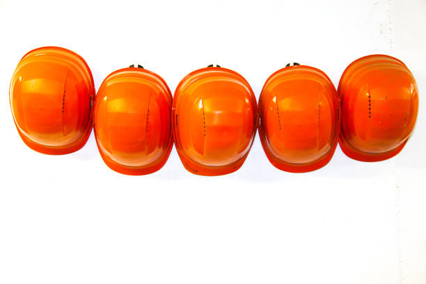 Orange safety helmets hang from hooks on the white wall.