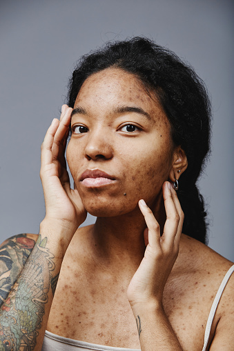 Vertical portrait of black young woman with no makeup looking at camera in studio, real beauty