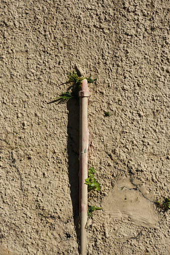 Part of a painted wall with a metal pipe on a sunny day.