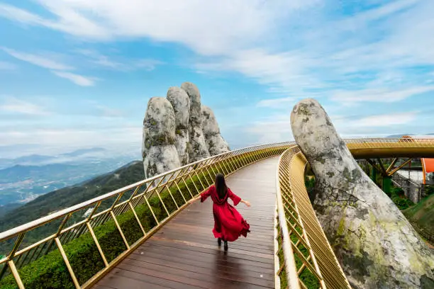 Photo of Young woman traveler in red dress enjoying at Golden Bridge in Bana hills, Danang Vietnam, Travel lifestyle concept