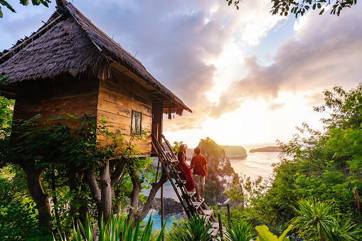 Young couple traveler enjoying and looking beautiful sunrise at the tree house in Nusa Penida island Bali, Indonesia