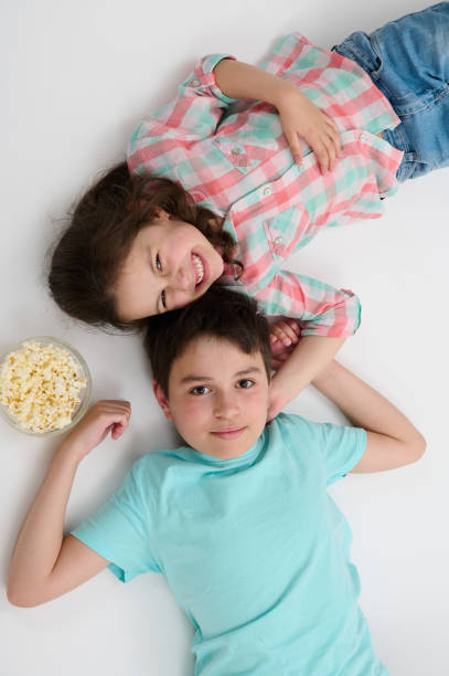 istock Top view adorable kids, mischievous sister and brother eating pop corn looking at camera, lying over white background. 1503228609