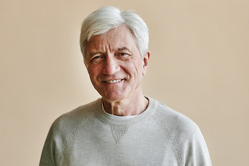 Waist up portrait of smiling senior man looking at camera against wall