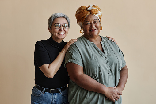 Waist up portrait of two senior women posing standing together and smiling at camera happily
