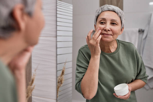 istock Smiling senior Asian woman looking in mirror and using face cream 1503230406