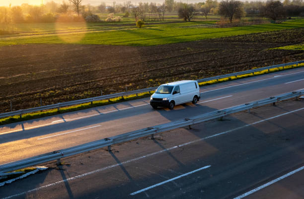 white delivery van on the highway. white modern delivery small shipment cargo courier van moving fast on motorway road to city urban suburb. the world's best transport of goods. - mini van imagens e fotografias de stock