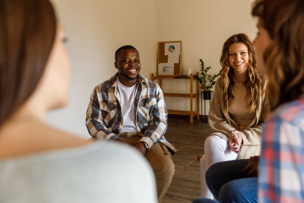 Young people having a laugh while casually chatting during a group therapy session stock photo