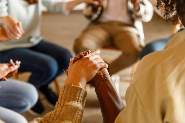 Diverse group of people sitting in circle and holding hands during a group therapy session