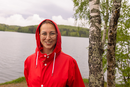 The happy woman in the red raincoat radiates positivity as she cherishes a moment of peace by the lake.