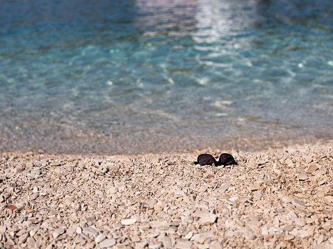 A pair of sunglasses on stones by the crystal blue waters of a seashore