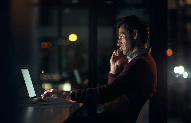 istock Phone call, night and businessman with a laptop in the office while working overtime on a deadline project. Communication, technology and professional male web developer doing research on a computer. 1503241496