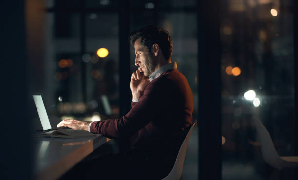 istock Phone call, overtime and man with a laptop in office while working on deadline project. Communication, technology and male web developer doing research on computer on a mobile conversation at night. 1503241497
