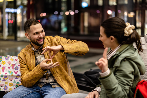 A young couple sitting on a bench at night, enjoying the cool breeze while using sign language to communicate