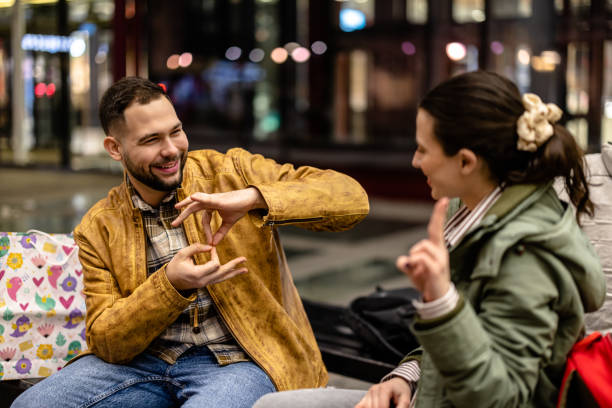 Young couple having a conversation in sign language A young couple sitting on a bench at night, enjoying the cool breeze while using sign language to communicate sign language stock pictures, royalty-free photos & images