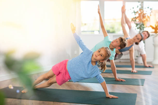 angenehmes kleines mädchen, das mit ihrer familie die seitliche plank-pose des yoga praktiziert - yoga good posture women little girls stock-fotos und bilder