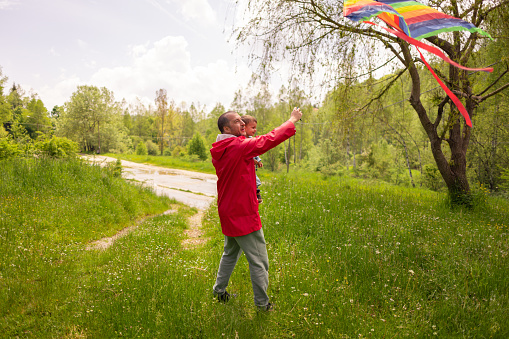 A father and his young son are enjoying a rainy day while flying a colorful kite in an open field.