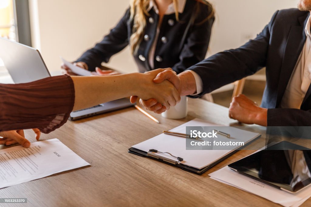 Interviewer and candidate shaking hands at the beginning of a job interview meeting Businesswoman sitting opposite interviewers and shaking hands at the beginning of a job interview meeting. Employment And Labor Stock Photo
