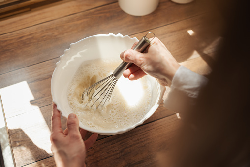 Close up of a wife cooking in kitchen, using whisk to stir different ingredients for liquid dough