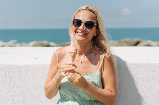 On the seashore, an attractive caucasian woman eats ice cream on a hot summer day.