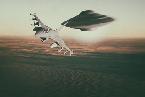 A modern F16 fighter jet streaks across the desert landscape whilst being pursued by a classic-style UFO. Scale model photography.