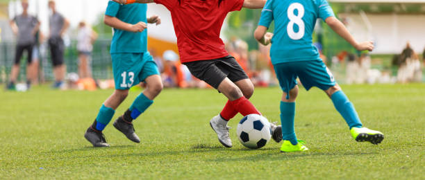 istock Junior competition between players running and kicking soccer. ball. Anonymous youth junior athletes in red and blue soccer shirts 1503279041