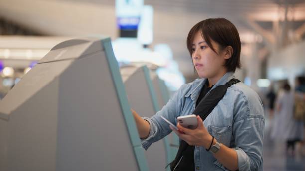 female tourist using automated self check-in counter in airport - airport airport check in counter ticket ticket machine imagens e fotografias de stock