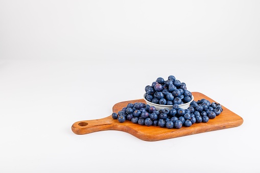 A wooden cutting board with an overflowing bowl of ripe blueberries atop