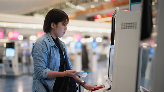 A female tourist is using an automated self check-in counter in an airport.