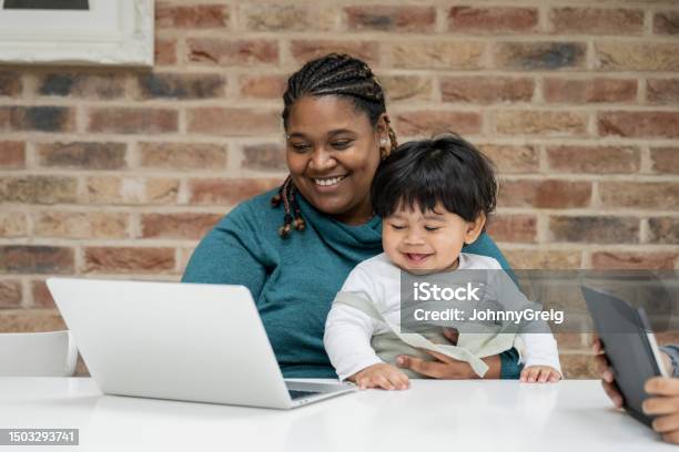 Cheerful Mother Multitasking At Home Stock Photo - Download Image Now - Child, Laptop, Mother