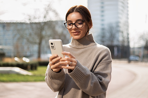 Beautiful woman student in eyeglasses using a phone in the street. Safe and happy.