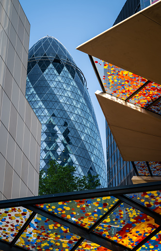London, UK:  The Gherkin skyscraper in the City of London with the colorful canopy above the entrance to 22 Bishopsgate in front.