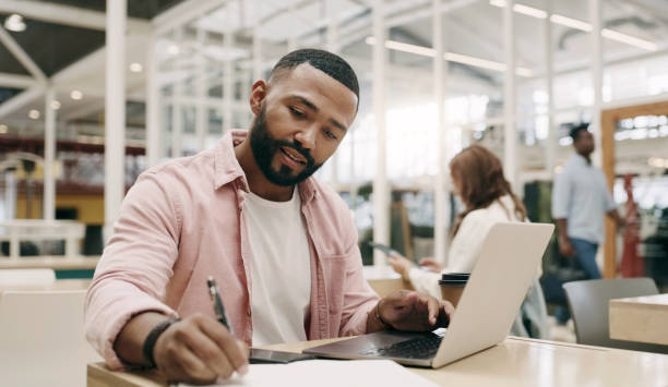 schreibend, kreativ und mann mit laptop im büro für geschäft, projekt oder forschung im startup. computer, notizen und afrikanischer professioneller texter, der an einem buch für die planung, den web-zeitplan und die e-mail arbeitet. - pen color image black book stock-fotos und bilder