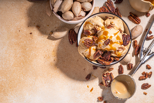 Pecan pie ice cream bowl. Traditional autumn spicy pecan caramel pie gelato taste, with rich caramel sauce and a lot of nuts, on kitchen table copy space