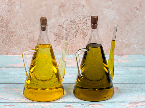 Two jugs of sunflower and olive oil, on bright blue wooden background