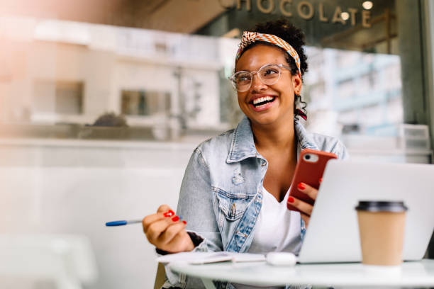 Happy female student sitting in a coffee shop, using a smartphone stock photo