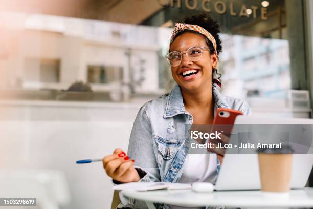 Happy Female Student Sitting In A Coffee Shop Using A Smartphone Stock Photo - Download Image Now