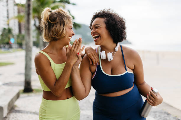 mulheres fitness rindo e se exaltando após um treino na praia - friendship women two people exercising - fotografias e filmes do acervo