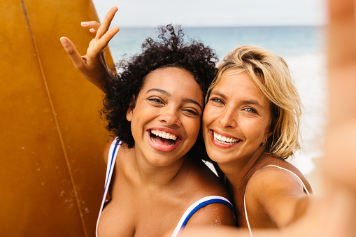 Fun beach memories are made as female surfers flash bright smiles for a selfie, encapsulating the carefree spirit and the thrilling experiences of their unforgettable surfing trip.
