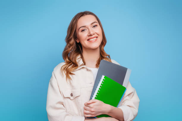 istock Happy girl student in bright clothes holding a notebook, notepad, a folder in her hands smiling and looking at the camera on a pink background, copy space for text 1503315745