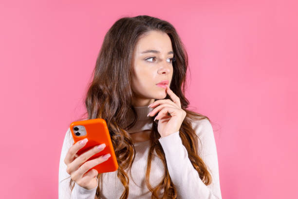 istock Lady looking on empty space deep thinking and holding mobile phone on the pink backgtound 1503316495