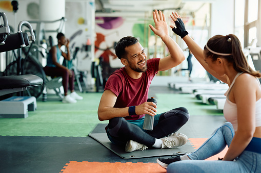 Happy athletic man giving high five to his female friend while relaxing after exercising in a gym.