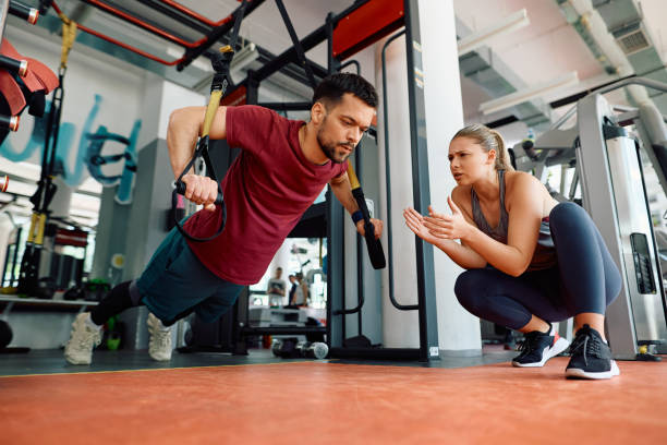 istock Athletic man using suspension straps while exercising strength with coach's support in a gym. 1503324937