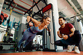 Happy athletic woman practicing push ups with trx straps in a gym.