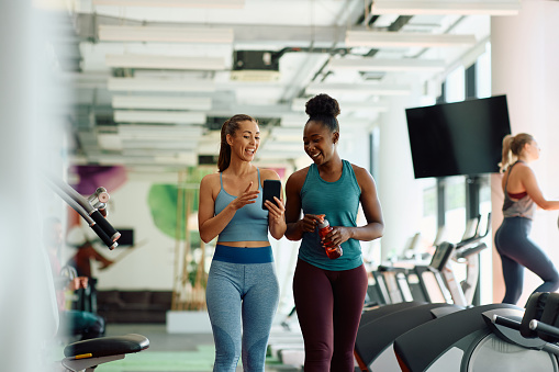 Cheerful female athletes using smart phone while working out in health club.