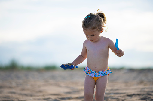 Little girl playing with sand on the beach at sunset.