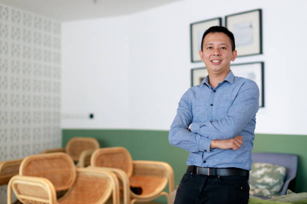 istock A portrait captures a young, confident Asian man standing with his arms folded and a bright smile on his face. He leans against a sofa, radiating positivity. 1503329101